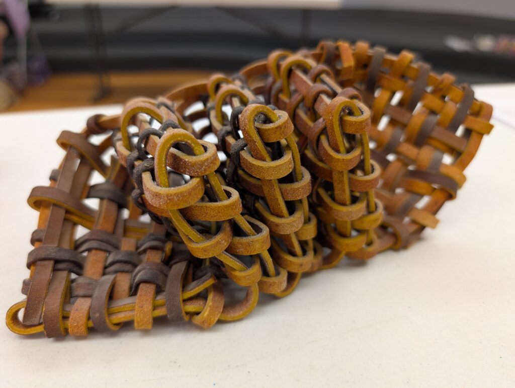 And abstract sculptural object made out of brown leather stripes plaited together in such a way that there's three folded sections in the middle.