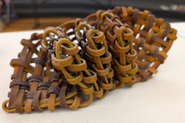 And abstract sculptural object made out of brown leather stripes plaited together in such a way that there's three folded sections in the middle.
