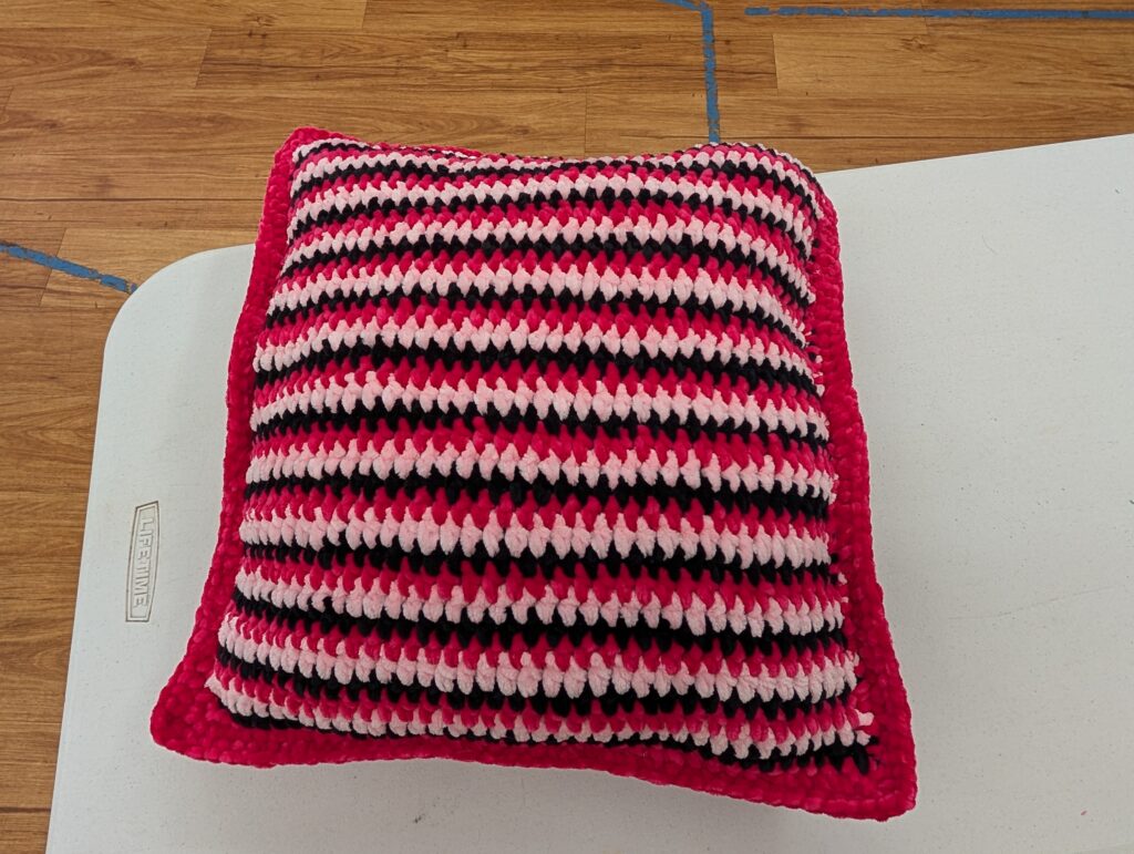 A hot pink, black, and white striped chenille pillow, trimmed in hot pink.