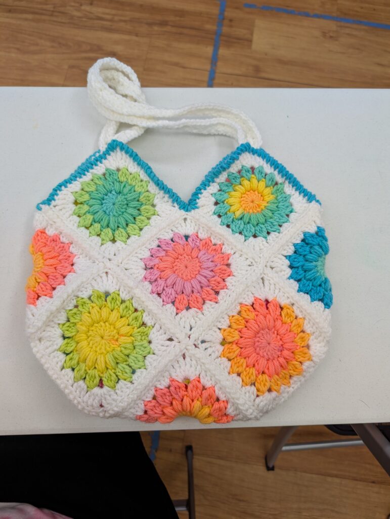 A bag made of crochet squares. The center of the squares are tropical shades of orange, pink, green, blue, and yellow on a white background.