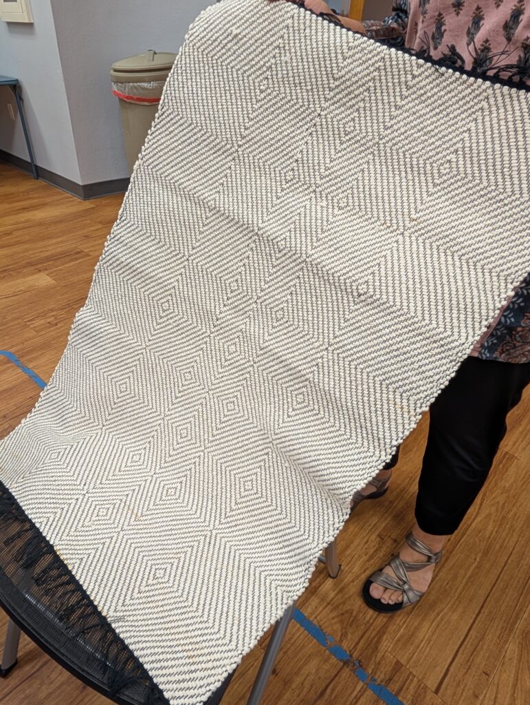 A woven rug approximately 2 x 3 feet. It is white with delicate black lines forming an angular geometric design.