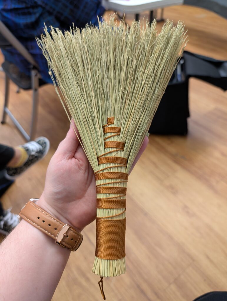 An angel wing style hand broom wrapped with orange brown thread.