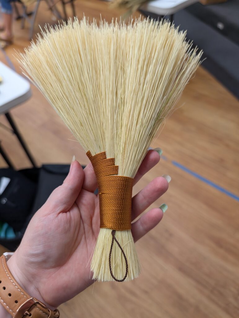 A turkey wing style hand broom made of tampico fiber and wrapped in orange brown thread.